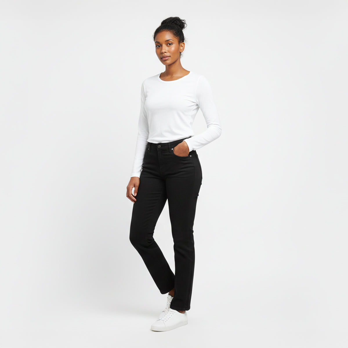 Woman wearing a white long-sleeve top and black jeans on a white background