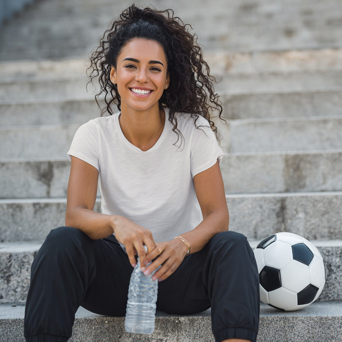 Woman sitting on steps with a water bottle and soccer ball